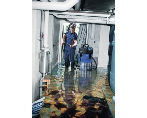 Mann benutzt einen Wassersauger in einem überfluteten Kellerraum