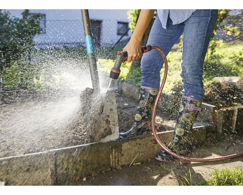 Eine Person reinigt eine Gartenschaufel mit einem Gartenschlauch.