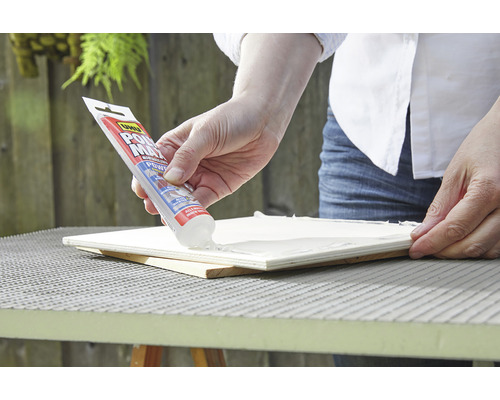 Une personne applique de la colle universelle UHU sur une surface en bois.