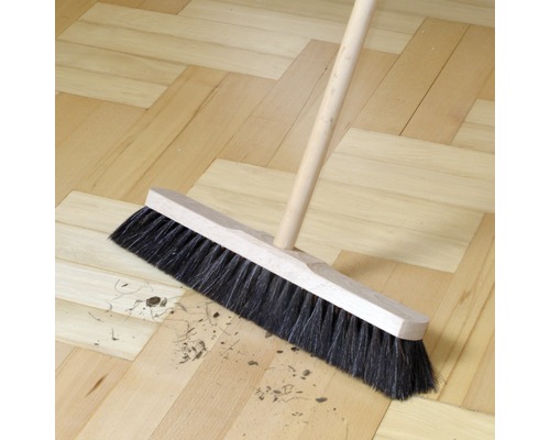 Balai de voirie avec manche en bois balayant la saleté sur un plancher en bois