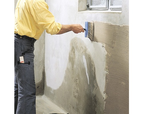 Un homme applique un produit d''étanchéité sur un mur avec une brosse plate