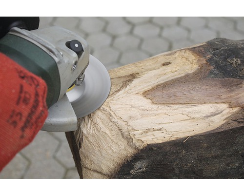 Eine Person bearbeitet ein Holzstück mit einem Winkelschleifer.