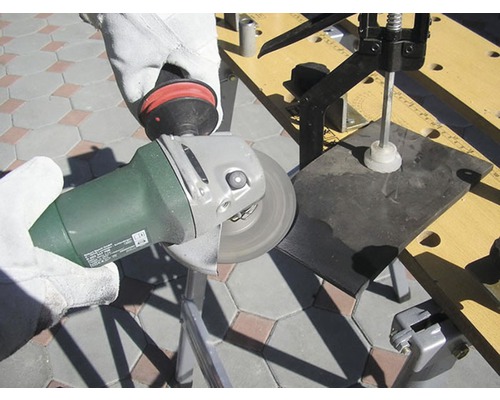 Eine Person schleift mit einem Winkelschleifer ein Werkstück auf einer Werkbank.