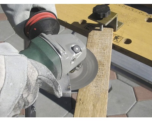 Eine Person schleift ein Holzbrett mit einem Winkelschleifer. Die Person trägt Handschuhe.