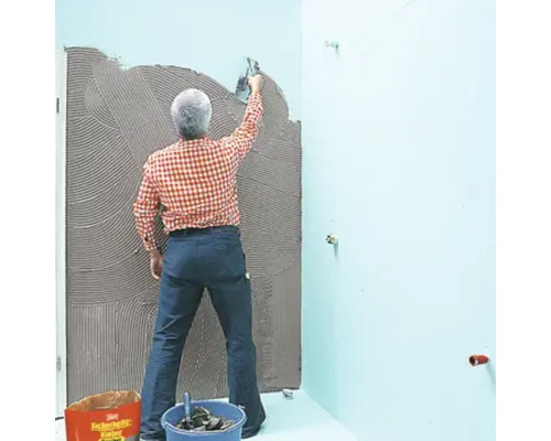 Un homme applique de la colle à carrelage sur un mur de salle de bains