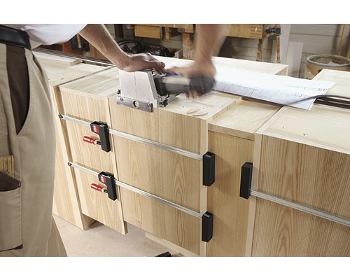 Un artisan travaille avec une fraise à lamelles sur un meuble en bois fixé avec des serre-joints.