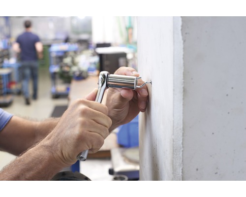 Eine Person befestigt einen Kippdübel mit einer Ratsche an einer Wand.