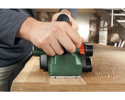 Un homme rabote une planche de bois avec un rabot électrique.