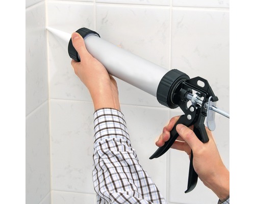 Application de mastic avec un pistolet à calfeutrer sur des carreaux