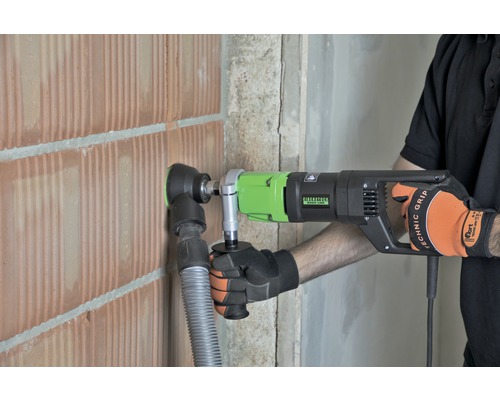 Ein Mann bohrt mit einer Kernbohrmaschine ein Loch in eine Ziegelwand.