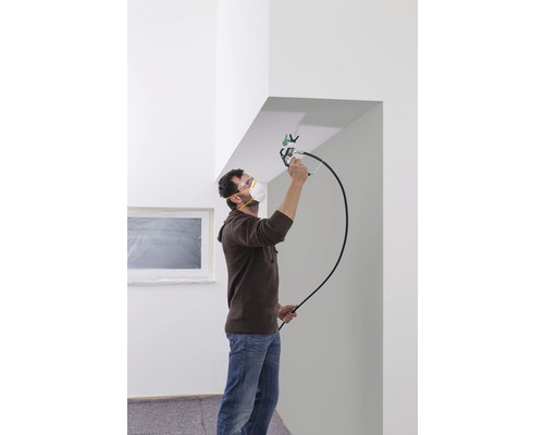 Un homme peint le plafond d''une pièce avec un pulvérisateur de peinture, portant un masque de protection et des lunettes de sécurité