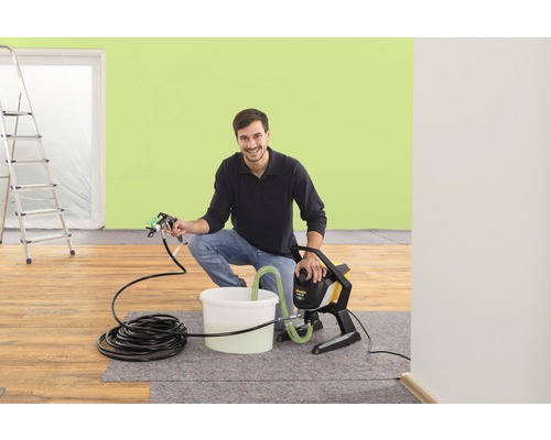 Un homme utilise un système de pulvérisation de peinture dans une pièce avec une échelle.