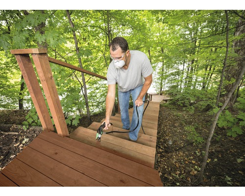 Homme avec masque respiratoire pulvérise un escalier en bois à l''extérieur avec un pulvérisateur de peinture