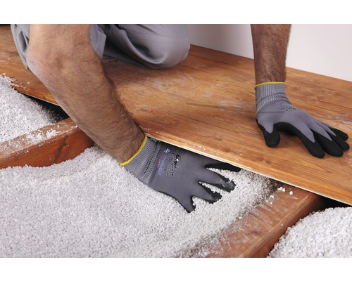 Un ouvrier portant des gants de travail répartit l''isolation en vrac sous un plancher en bois.