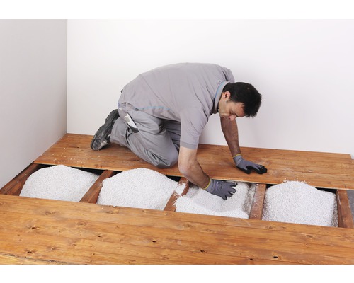 Un homme verse de l''isolant en vrac dans un plancher en bois