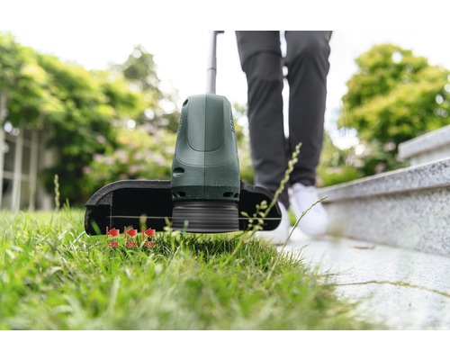 Une débroussailleuse coupe l''herbe au bord d''une pelouse