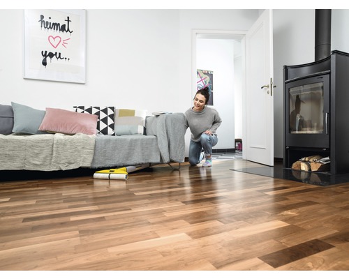 Une femme utilise un robot laveur jaune dans un salon avec un canapé, une cheminée et un plancher en bois.