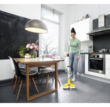 Une femme nettoie la cuisine avec un balai électrique
