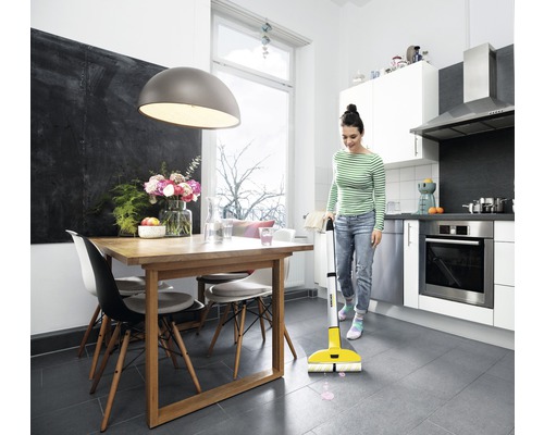 Une femme nettoie la cuisine avec un balai électrique