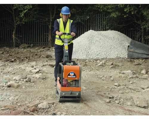 Ouvrier du bâtiment compactant le sol avec une plaque vibrante.