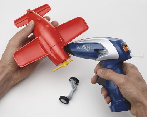 Une personne utilise un pistolet à colle chaude pour réparer un avion jouet rouge