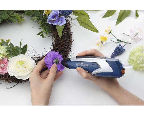 Une femme fixe des décorations sur une couronne à l''aide d''un pistolet à colle chaude