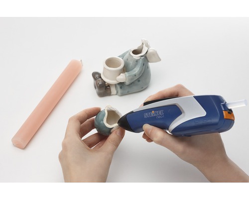 Person repariert Keramikfigur mit Heissklebepistole