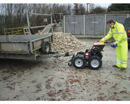 Une personne utilise un mini-transporteur tirant une remorque. Un tas de pierres est visible à l''arrière-plan.