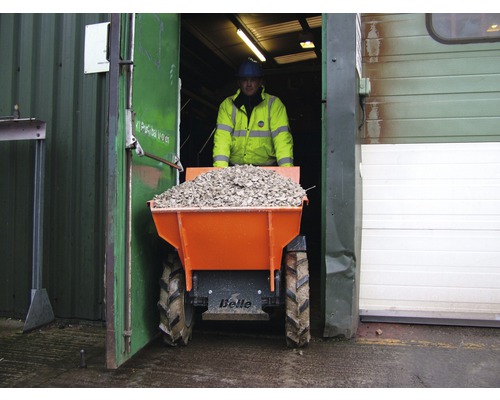 Un homme transporte du gravier avec un dumper hors d''un bâtiment.