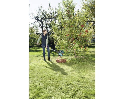 Une femme récolte des pommes avec un cueille-fruits et un panier dans le jardin.