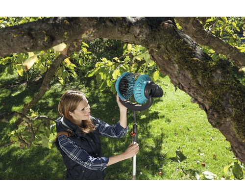 Une femme utilise un cueille-fruits dans un jardin sous un arbre.