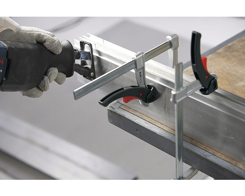 Eine Säbelsäge schneidet ein Metallprofil, das mit Schraubzwingen fixiert ist.