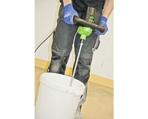 Un homme mélange des matériaux avec un mélangeur de peinture dans un seau.