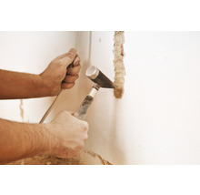 Un artisan creuse une rainure dans un mur avec un marteau et un burin.