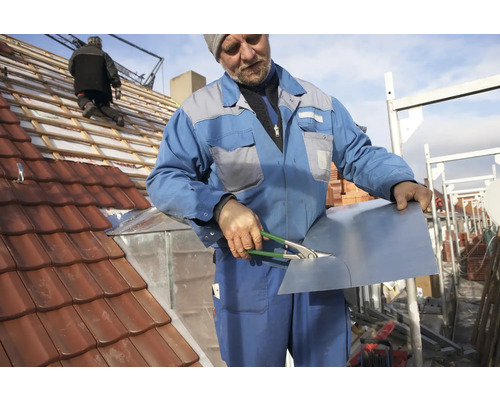 Ein Handwerker schneidet ein Blechteil auf einem Dach mit Dachziegeln.