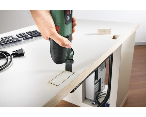 Une personne utilise un outil multifonction pour percer un trou dans un plateau de table.