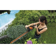 Une femme taille une haie avec un taille-haie dans le jardin