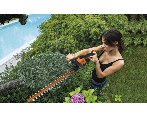 Frau schneidet Hecke mit einer Heckenschere im Garten