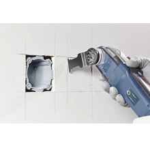 Un outil électrique oscillant découpe un évidement dans un mur.