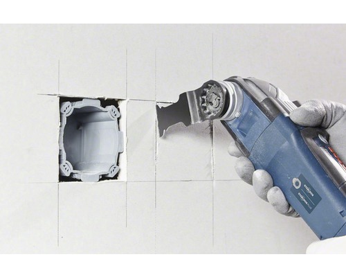 Un outil électrique oscillant découpe un évidement dans un mur.
