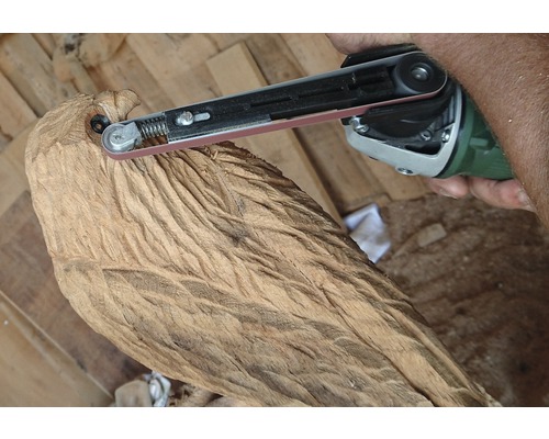Handwerker bearbeitet eine geschnitzte Holzfigur mit einem Bandschleifer.