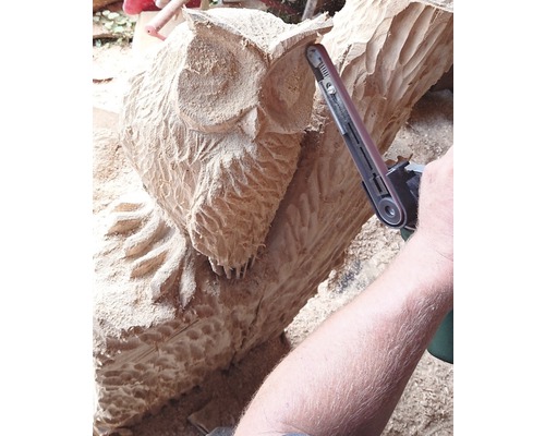 Eine geschnitzte Holzeule wird mit einem Bandschleifer bearbeitet.