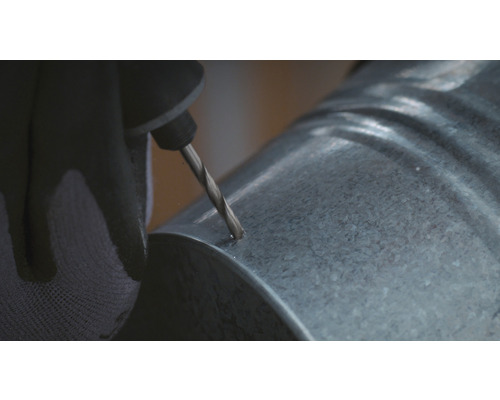 Une personne perce un trou dans un tube galvanisé.