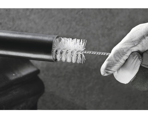 Une main avec un gant de travail nettoie un tuyau avec une brosse de nettoyage.