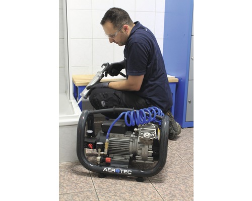 Un artisan utilise un pistolet à cartouche et un compresseur dans la salle de bains.