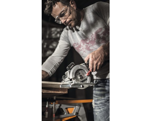 Un homme scie une planche de bois avec une scie circulaire sur un établi