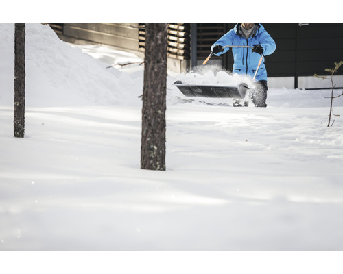 Une personne déblaie la neige avec une pelle à neige devant une maison.