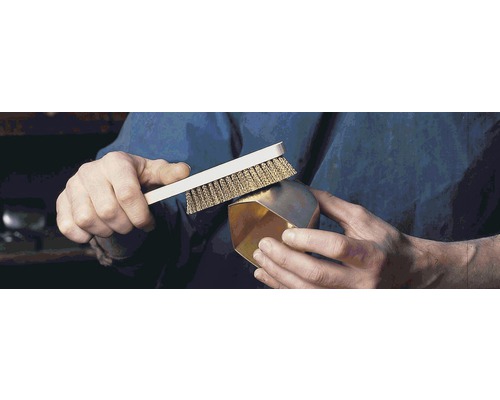 Eine Person reinigt einen goldenen Gegenstand mit einer Drahtbürste.