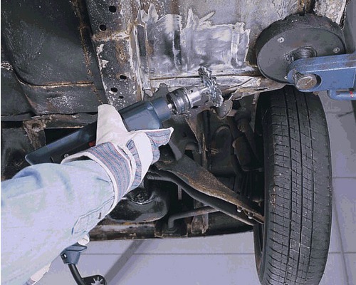 Eine Person entfernt Rost von einem Fahrzeug mit einer Entrostungsbürste.
