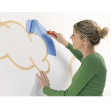 Femme peignant un nuage sur un mur avec un rouleau à peinture.